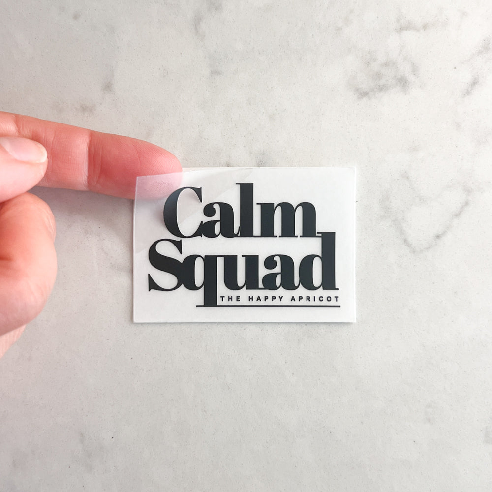 Hand holding a 'Calm Squad' sticker with 'The Happy Apricot' on a marble background