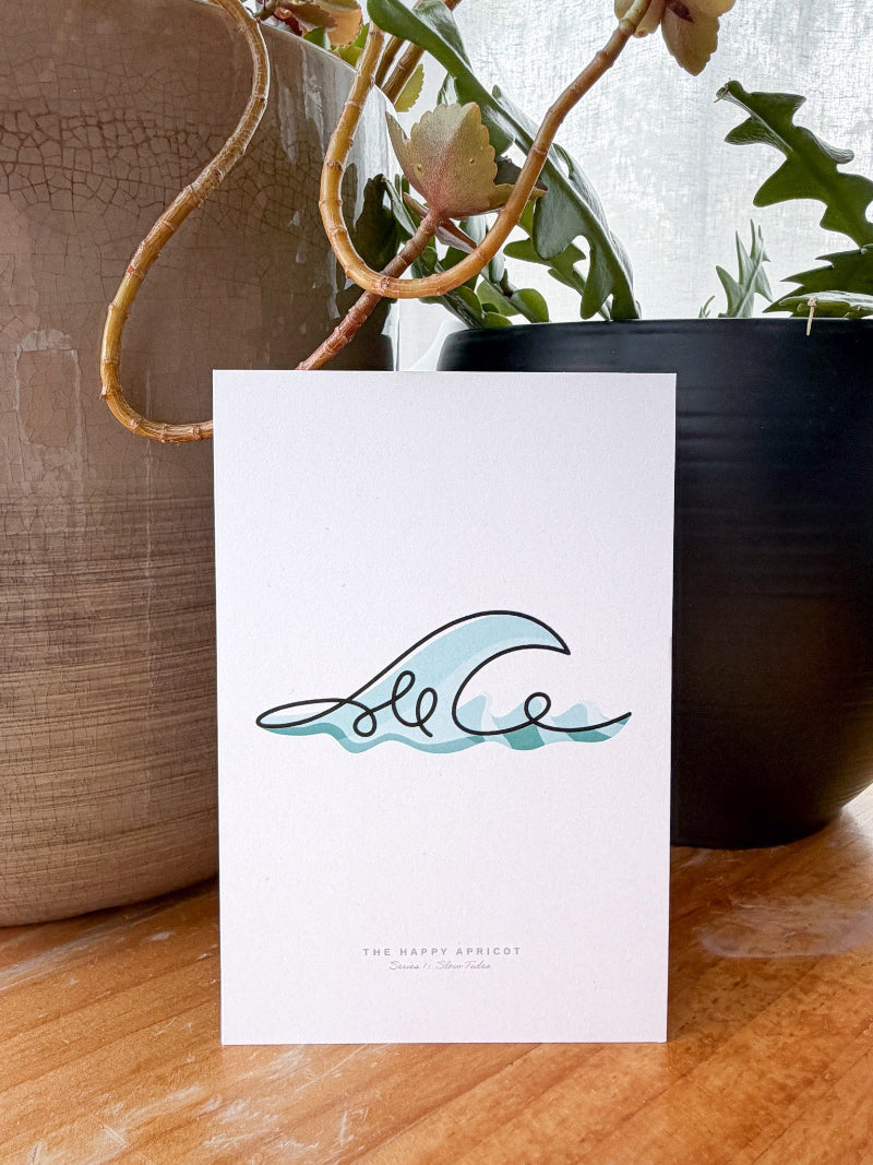 A white card featuring a minimalist black and light blue wave illustration with the text 'The Happy Apricot' at the bottom, displayed on a wooden surface with potted plants in the background.