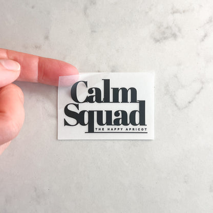 Hand holding a 'Calm Squad' sticker with 'The Happy Apricot' on a marble background