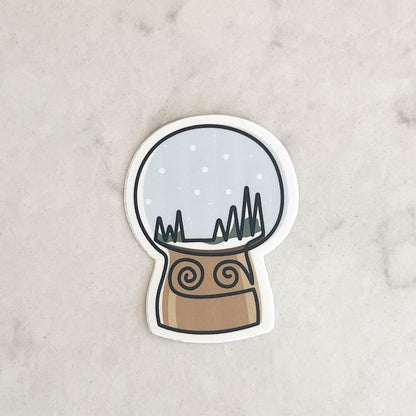 Sticker of a snow globe with a mountain scene on a light gray background